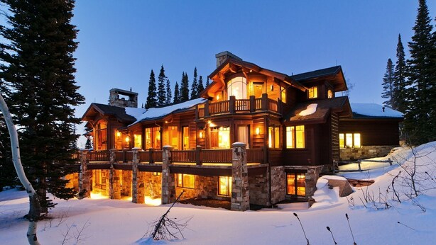 Un grand chalet en bois à plusieurs étages, doté d’un balcon, entouré de neige et d’arbres.