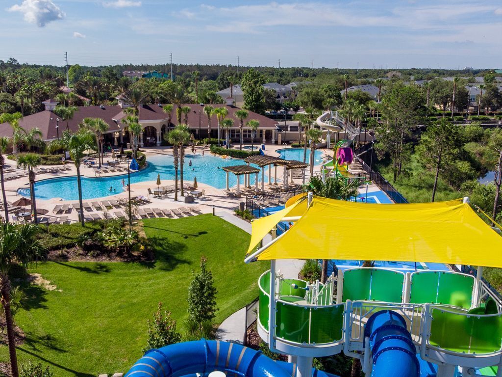 Un resort con múltiples piscinas, un tobogán acuático y un amplio césped bien cuidado.