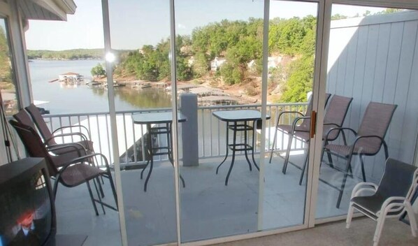 A balcony with a glass door, outdoor furniture, and a view of a lake and trees.