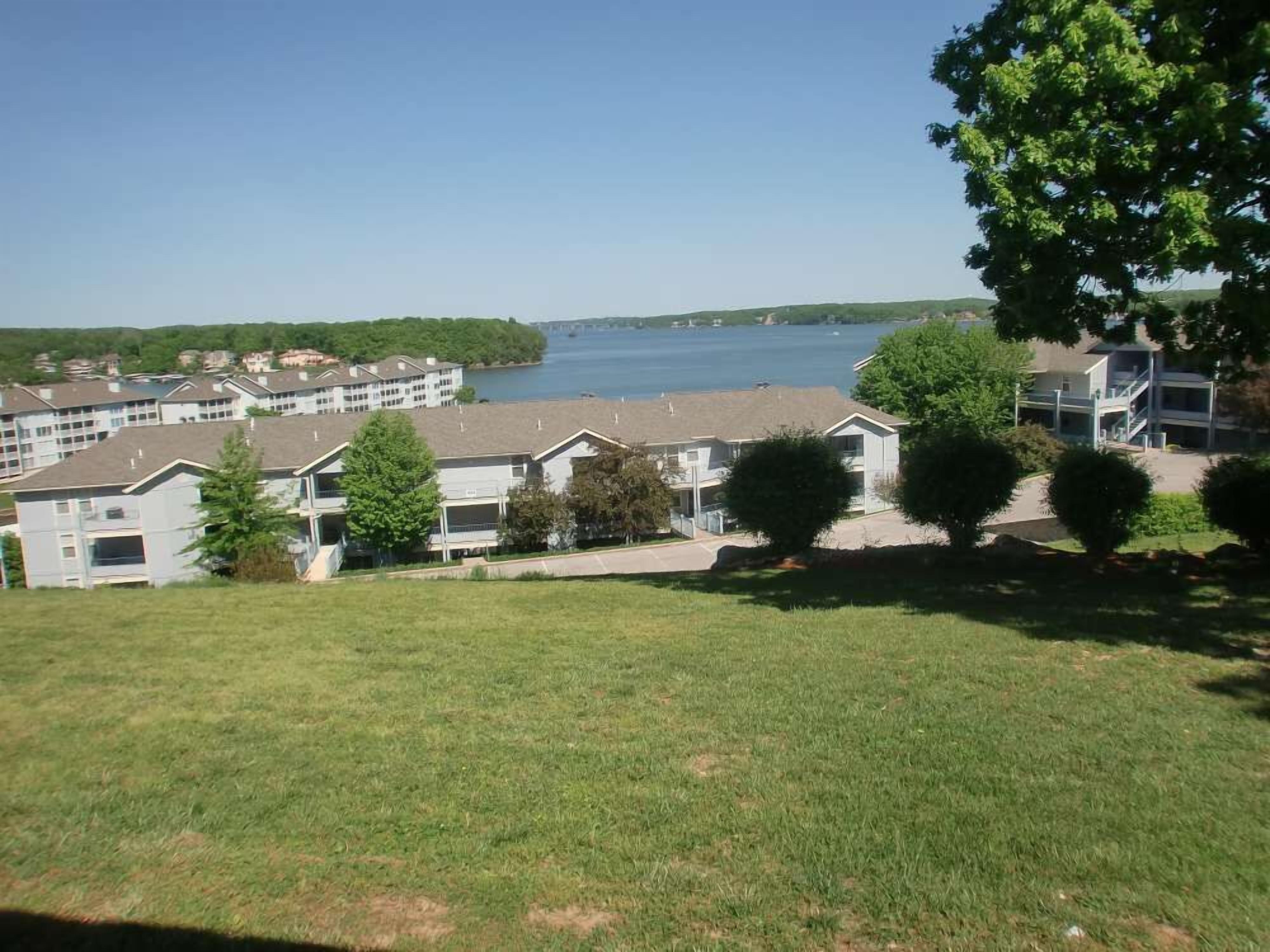 A residential area with multiple apartment buildings, a grassy foreground, and a lake in the background.