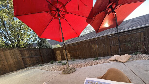 Un'area patio con un ombrello rosso, una recinzione in legno e una rivista intitolata "MOAB HAPPENINGS" sul terreno.