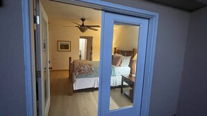 Una camera da letto con un letto, un comodino, una ventola a soffitto e una porta che dà su un'altra stanza.