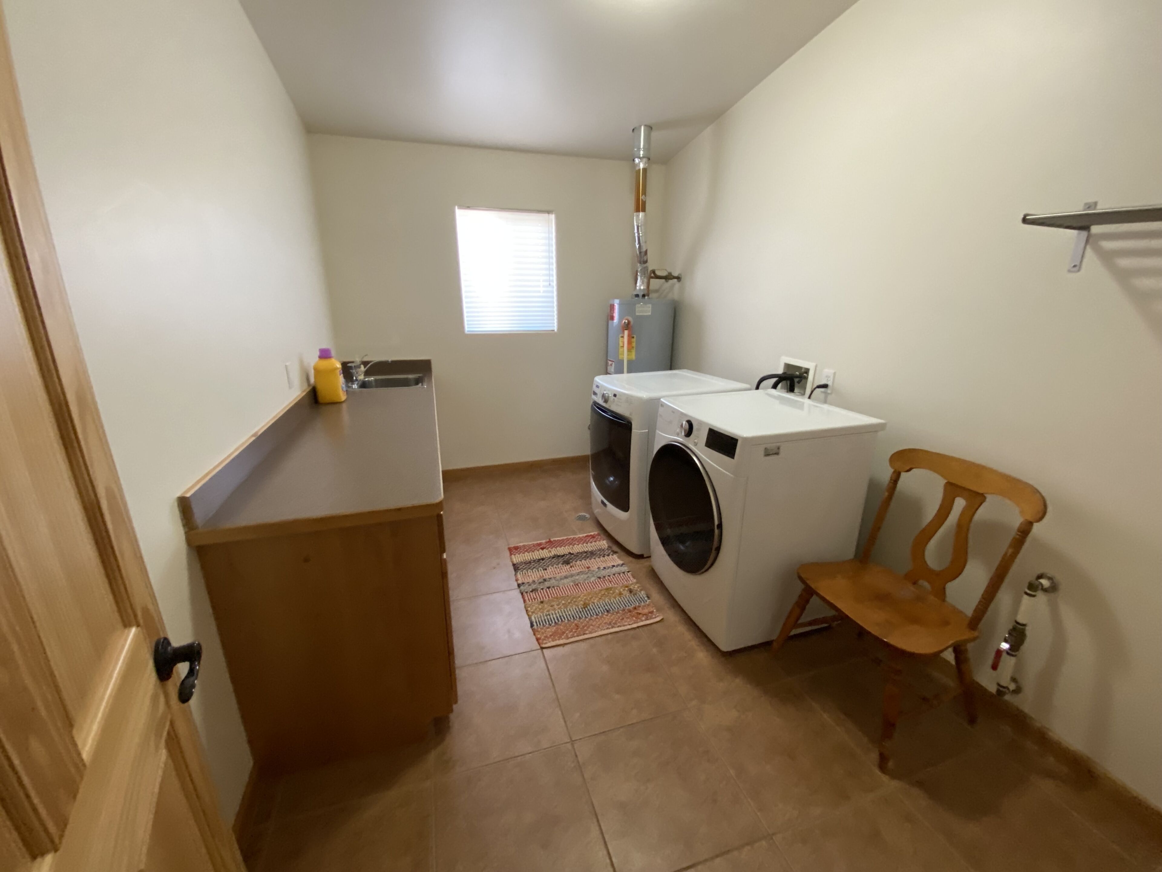 A laundry room with two washing machines, a small sink, and a wooden chair.