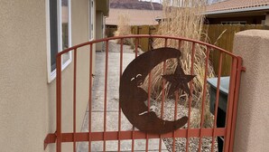 Un cancello in metallo con decori a mezzaluna e stella, un vialetto in cemento e una recinzione in legno.
