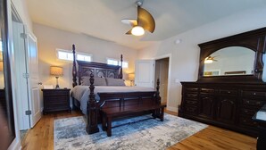 Een slaapkamer met een hemelbed, een houten dressoir en een plafondventilator.