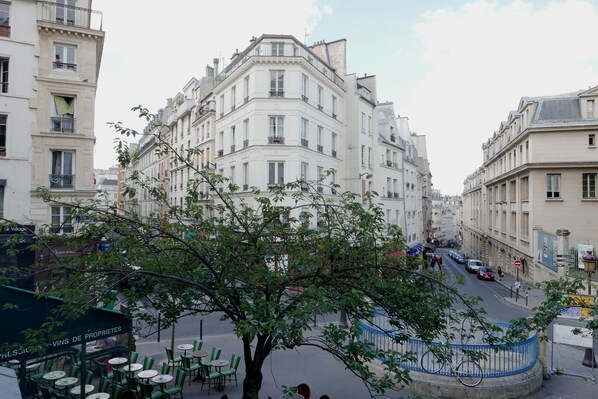A street view with a tree in the foreground, buildings on either side, and a café with outdoor seating.