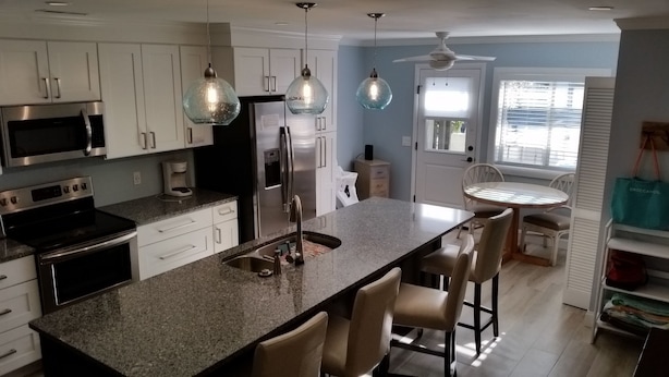 A kitchen with white cabinets, stainless steel appliances, a granite countertop, and pendant lighting. - 604 Tennismaster, OWNER Mgmt, Beach Locker, Handicap & Family Friendly (Hilton Head Island)