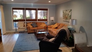 A living room with a sofa, armchair, and coffee table. There are two windows with blinds, a lamp, and a painting on the wall. - 604 Tennismaster, OWNER Mgmt, Beach Locker, Handicap & Family Friendly (Hilton Head Island)