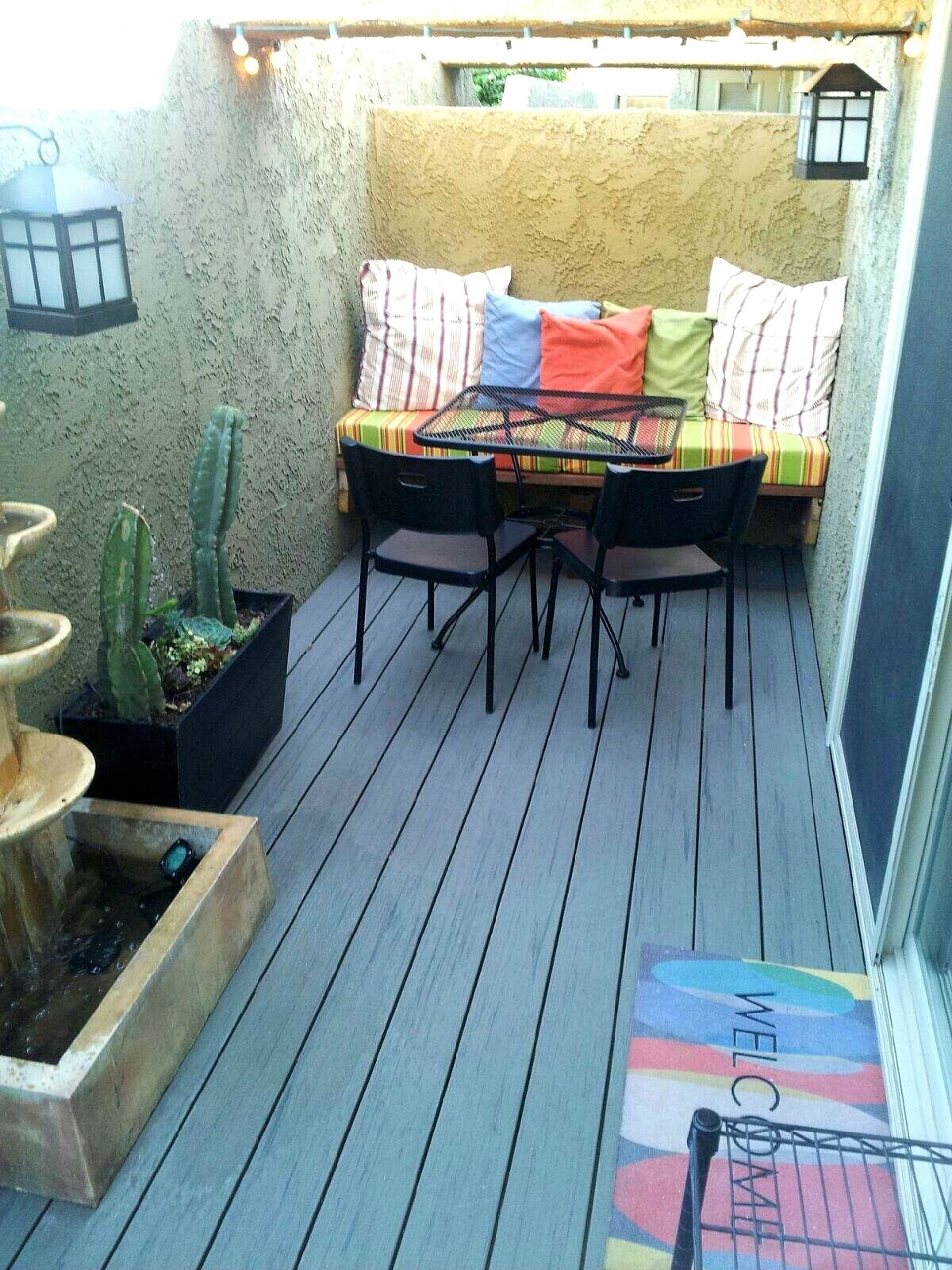 Un pequeño patio con una mesa y sillas, un banco acolchado y cactus en macetas.