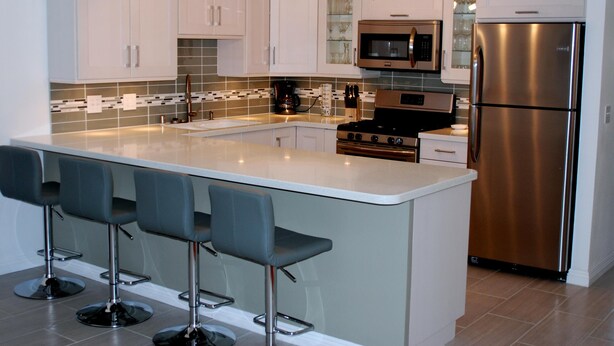A modern kitchen with a central island, bar stools, stainless steel appliances, and white cabinetry.