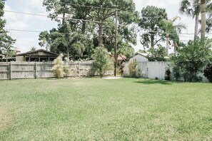 Un patio trasero con césped, una valla de madera, un árbol pequeño y una casa al fondo.