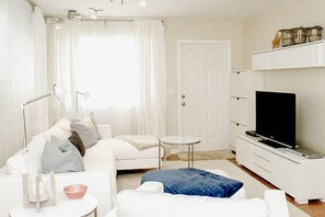 A modern living room with a white sofa, a coffee table, a TV on a stand, and a door with a white frame.