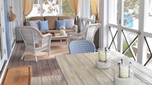 Eine überdachte Veranda mit einem Holztisch, Korbstühlen und einer Couch mit Kissen.