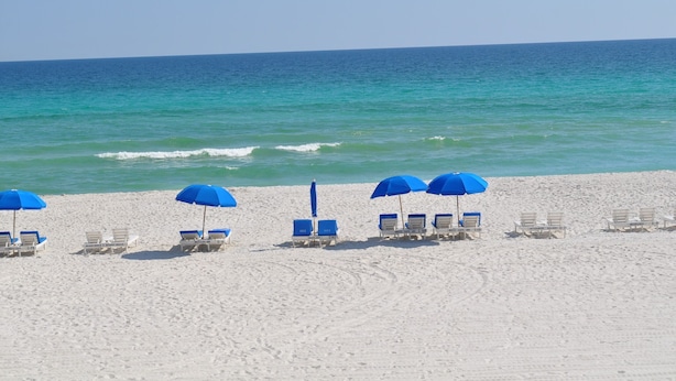 Ein Strand mit weißem Sand und blauen Sonnenschirmen.