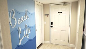Een hal met een muurschildering getiteld 'Beach Life', een witte deur en een lichtgekleurde vloer.