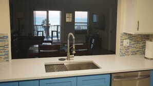 Een keuken met een roestvrijstalen spoelbak, blauwe kastjes en uitzicht op de oceaan door grote ramen.