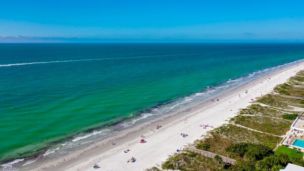 Een strand met een lange zandvlakte, enkele mensen en een helder uitzicht op de oceaan.
