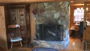 A cozy cabin interior with a stone fireplace, wooden walls, and a high ceiling.