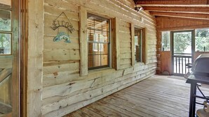 A log cabin with a covered porch, large windows, and a welcome sign.