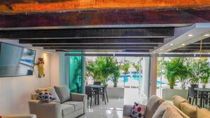 Un moderno vestíbulo de hotel con zona de estar, vista a la piscina y plantas de interior.