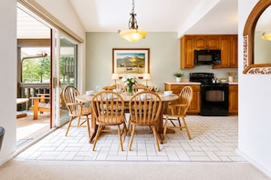 A dining area with a table, chairs, and a painting. There is a kitchen with wooden cabinets and appliances.