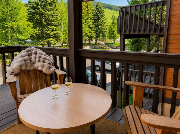 A wooden deck with a round table and two chairs, two glasses of white wine, and a fur throw on one chair.