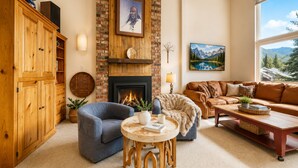 Una sala de estar acogedora con chimenea, un sillón azul, un sofá marrón y vistas a la montaña a través de la ventana.