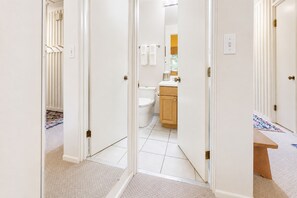 Pasillo que conduce a un baño con inodoro, lavamanos y espejo.