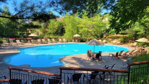 A swimming pool with lounge chairs and umbrellas, surrounded by trees and a brick patio. - RENOVATED- Ski in&out /Walk to village/ Corner Unit/Pool (summer) Sunny/Views/AC (Mont-Tremblant)