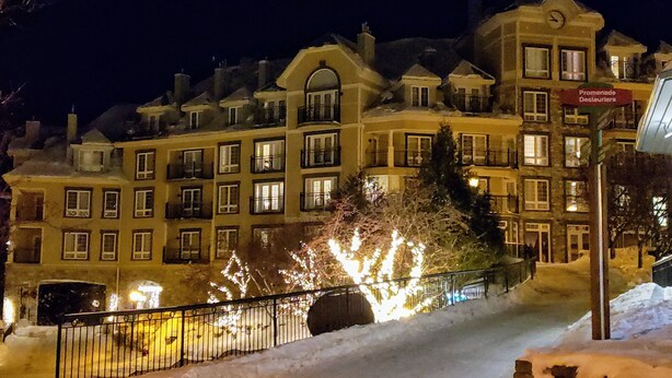 A multi-story hotel with illuminated windows and a snow-covered exterior. - RENOVATED- Ski in&out /Walk to village/ Corner Unit/Pool (summer) Sunny/Views/AC (Mont-Tremblant)