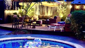 A pool with clear water and floating decorations, surrounded by outdoor seating and a bamboo backdrop. - Updated Furnished Cottage With New BBQ, spa, and Pool - small pet considered (Chico)