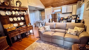 A living room with a sofa, wooden cabinet, and a kitchen in the background. - Updated Furnished Cottage With New BBQ, spa, and Pool - small pet considered (Chico)