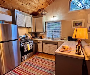 A compact kitchen with a refrigerator, stove, oven, and a window with blinds.