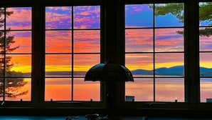 A room with large windows offering a view of a sunset over a body of water. - Acadia National Park-Oceanfront Cottage-Views of Cadillac Mountain & Acadia-Pets (Lamoine)