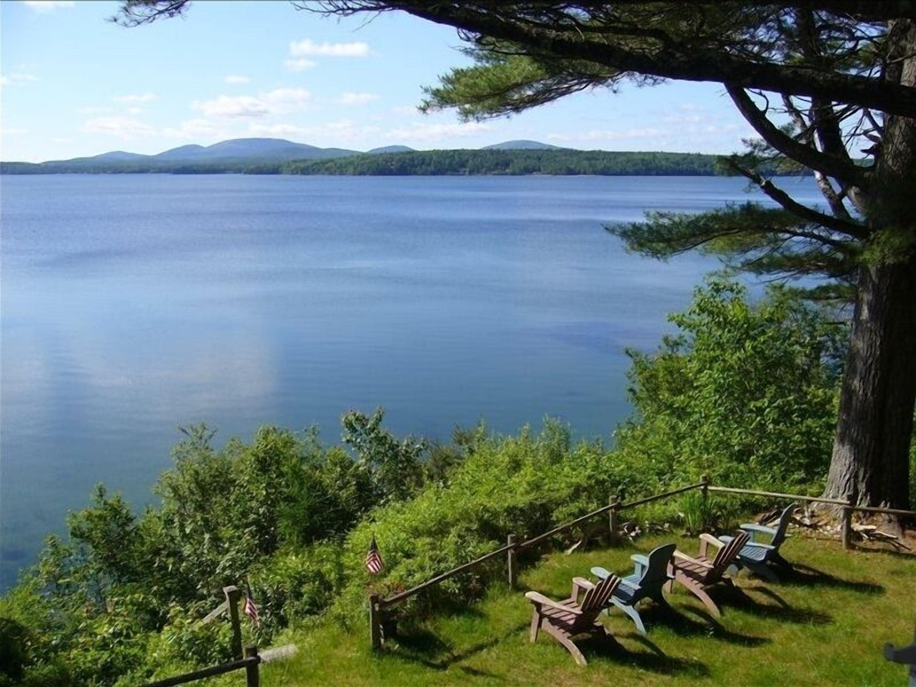 A lakeside view with a wooden deck and Adirondack chairs overlooking the water.