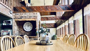 A wooden dining table with chairs, a clock, and a brick wall with a fireplace. - Rustic retreat -So much fun - log playground, hot tub, concrete game court (Crystola)