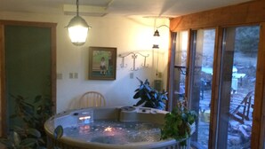 A room with a hot tub, a chair, a table, and a large window with a view of the outdoors. - Rustic retreat -So much fun - log playground, hot tub, concrete game court (Crystola)