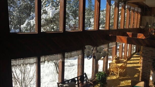 A cozy cabin with large windows offering a view of snow-covered trees. Inside, there's a wooden bench and a dining area with chairs and a table. - Rustic retreat -So much fun - log playground, hot tub, concrete game court (Crystola)