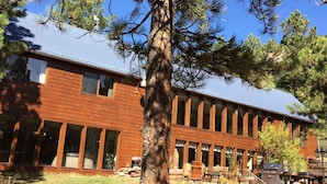 A building with a brick facade and large windows, surrounded by a grassy area and trees. - Rustic retreat -So much fun - log playground, hot tub, concrete game court (Crystola)