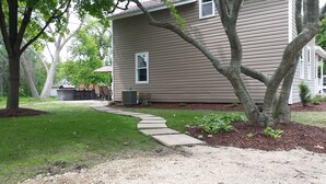 A residential house with a paved driveway, a small garden, and a patio area with outdoor furniture. - Only 2 blocks to beach, one block to kids corner, over half an acre! (South Haven)