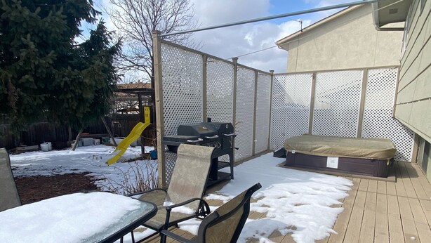 Une terrasse en bois avec des meubles d’extérieur, un barbecue et un espace clos comprenant un arbre et un toboggan jaune.