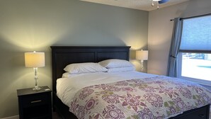 Un lit bien fait, recouvert d’une couvre-lit à motifs floraux, avec deux lampes de chevet, une tête de lit en bois foncé et une fenêtre équipée de stores.