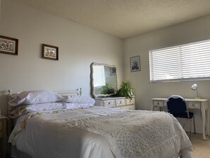 A bedroom with a bed, dresser, desk, chair, and a window with blinds.
