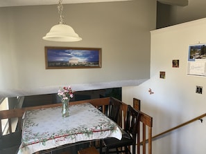 A dining area with a table set for four, a vase with flowers, a framed picture on the wall, and a calendar.