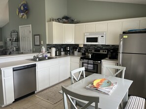 Een moderne keuken met witte kasten, roestvrijstalen apparatuur en een eethoek met een tafel en stoelen.