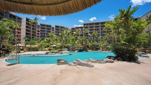 Un complexe hôtelier doté d’une piscine centrale, de palmiers et d’un immeuble à plusieurs étages avec des balcons.