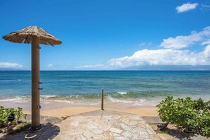 Blick auf einen Strand mit einem Reetdachschirmchen, einem Steinweg und einem klaren, blauen Himmel.