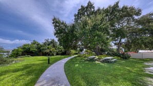 Ein gewundener Betonweg führt zu einer Picknickzone mit Bänken und einem Tisch, umgeben von üppiger Vegetation und Bäumen.