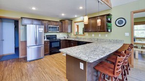 A modern kitchen with granite countertops, stainless steel appliances, wooden cabinets, and a built-in island with bar stools. - WolfRun Lake View Chalet, 200 feet from Lake, Hottub (Albrightsville)