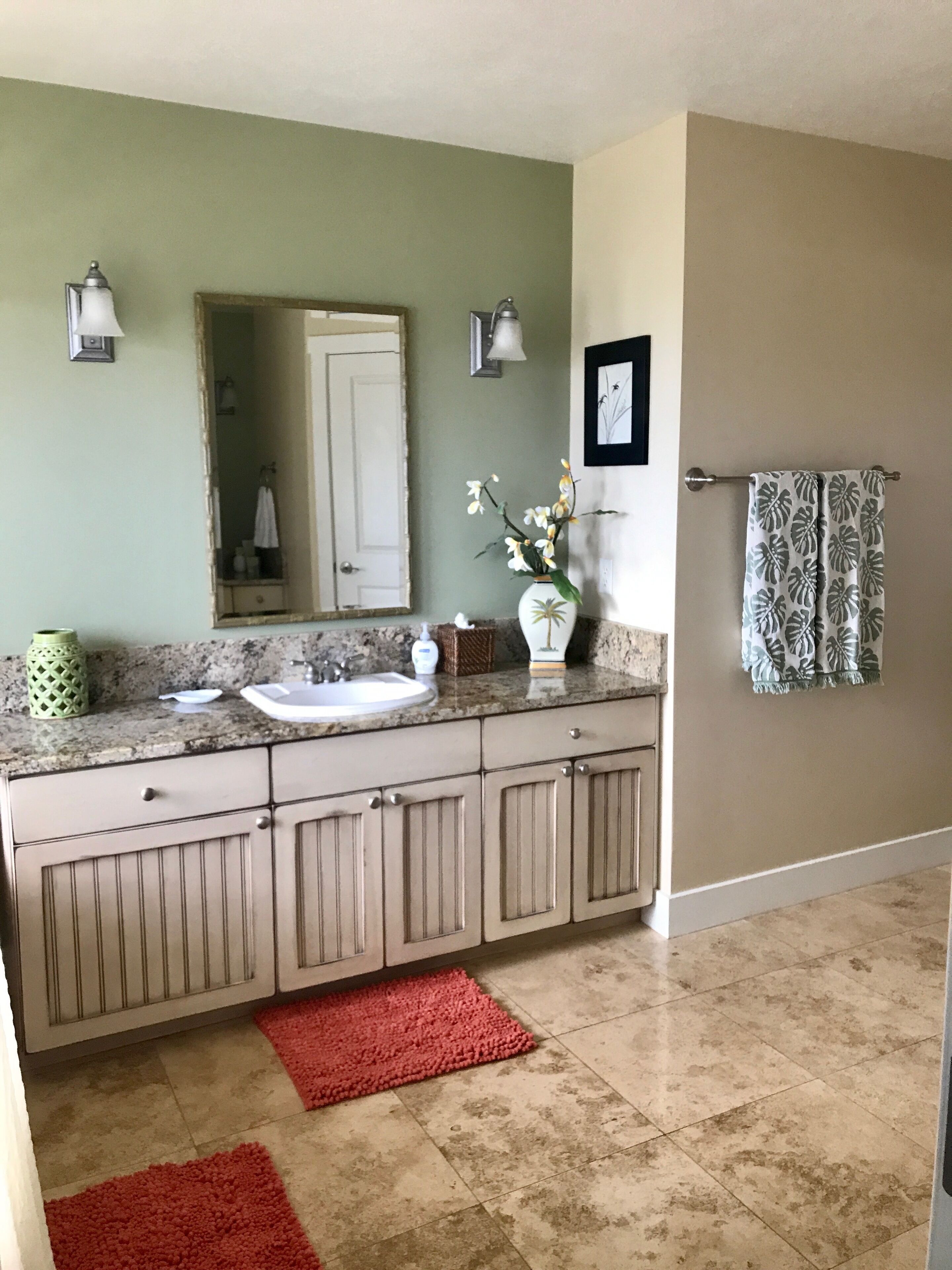 A bathroom with a granite countertop, a sink, a mirror, a towel rack, and a red bath mat.